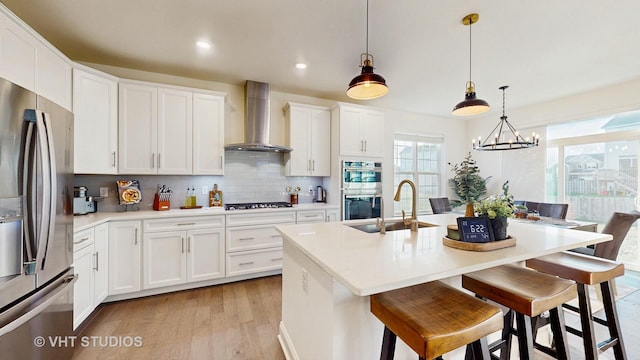 kitchen featuring tasteful backsplash, light wood-type flooring, wall chimney range hood, stainless steel appliances, and a sink