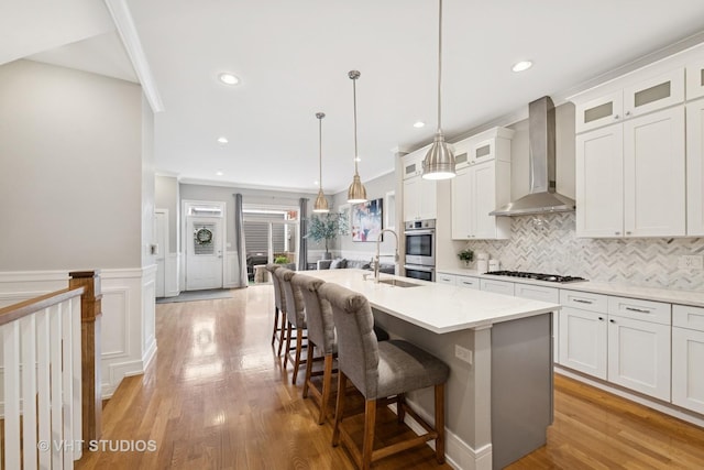 2733 N Maplewood Ave, Chicago, IL 60647 - kitchen featuring light wood-type flooring, wall chimney exhaust hood, an island with sink, and a sink