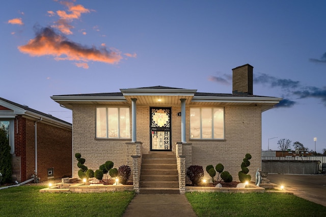 view of front of house featuring a lawn, a shingled roof, a chimney, and brick siding