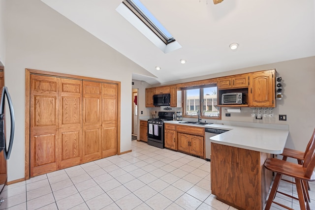kitchen with vaulted ceiling with skylight, a sink, light countertops, a peninsula, and appliances with stainless steel finishes