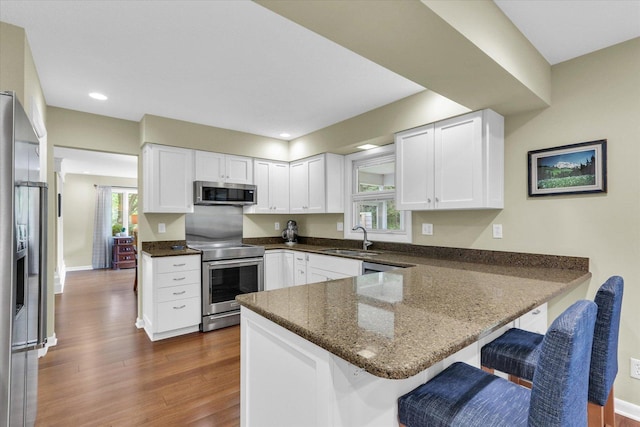 1104 Parkview Dr, Mahomet, IL 61853 - kitchen featuring appliances with stainless steel finishes, a peninsula, white cabinets, a breakfast bar, and dark wood-style flooring