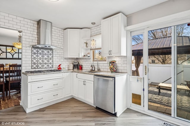kitchen with wall chimney range hood, open shelves, decorative backsplash, stainless steel appliances, and a sink