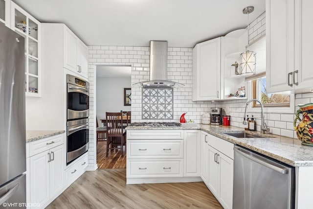 kitchen with wall chimney exhaust hood, a sink, stainless steel appliances, light wood-style flooring, and decorative backsplash