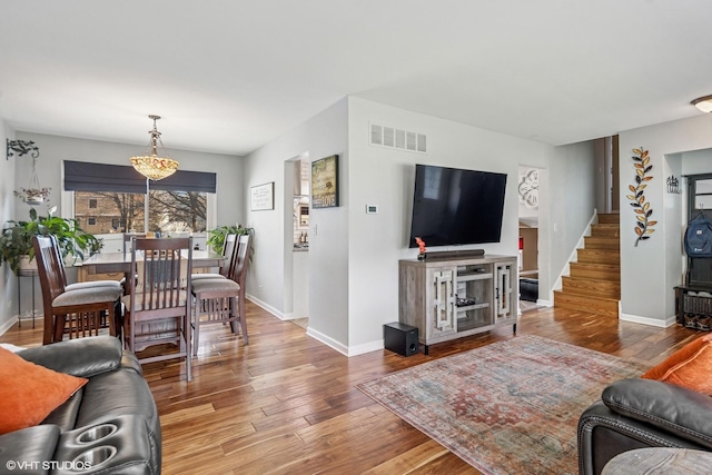living room with stairway, visible vents, hardwood / wood-style flooring, and baseboards