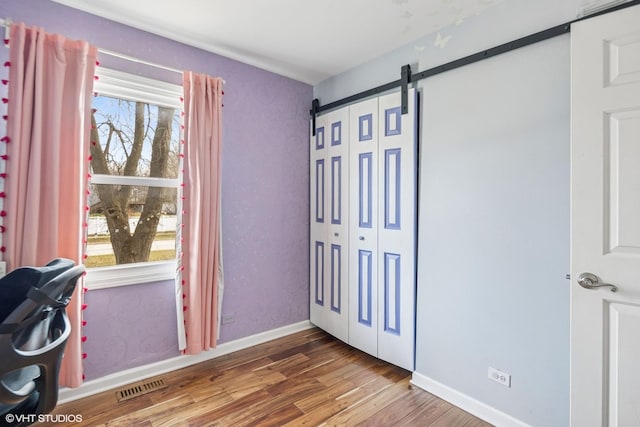 bedroom with a closet, visible vents, a barn door, wood finished floors, and baseboards