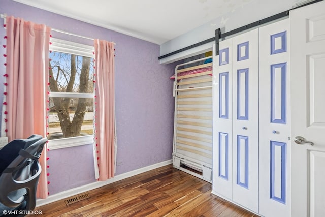 unfurnished bedroom with visible vents, baseboards, a barn door, and wood finished floors