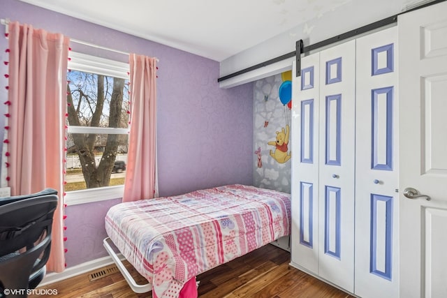 bedroom with a closet, a barn door, baseboards, and wood finished floors