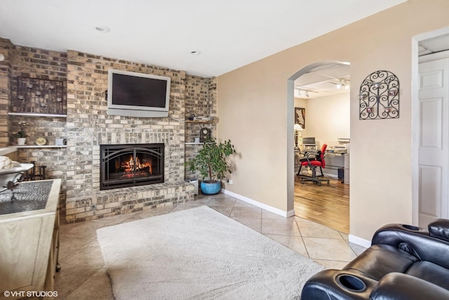living area featuring arched walkways, tile patterned flooring, a brick fireplace, and baseboards