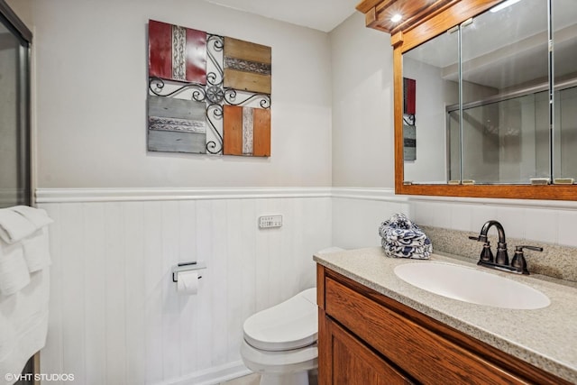 bathroom featuring toilet, wainscoting, a shower with shower door, and vanity