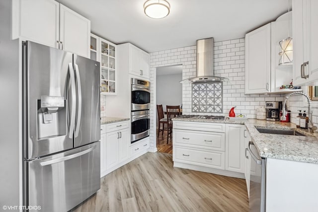 kitchen with light wood-type flooring, backsplash, wall chimney exhaust hood, stainless steel appliances, and a sink