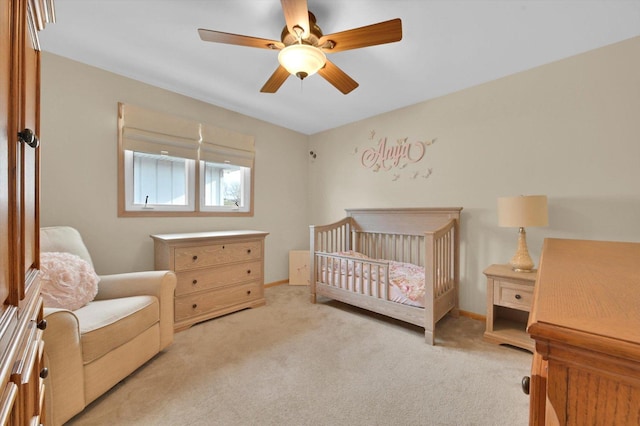 bedroom with light carpet, a ceiling fan, and a crib