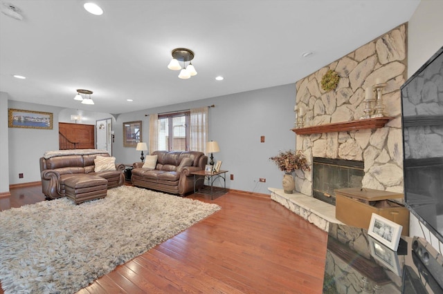 living area with baseboards, wood finished floors, a stone fireplace, and recessed lighting