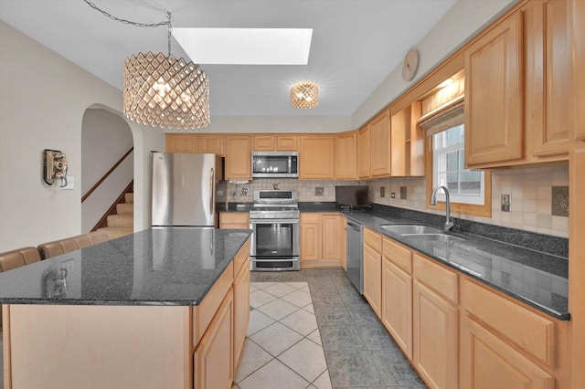 kitchen with a sink, a skylight, decorative backsplash, light brown cabinetry, and appliances with stainless steel finishes