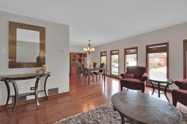 living area featuring baseboards, a chandelier, wood finished floors, and visible vents