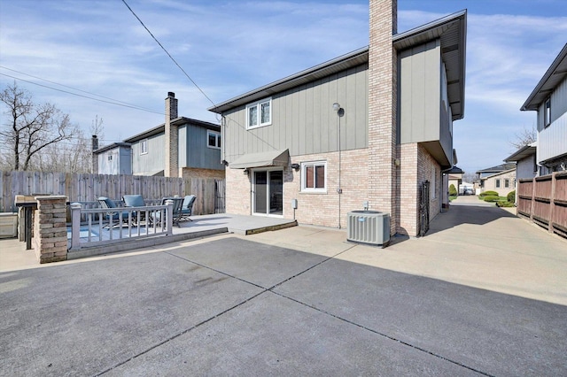 rear view of house featuring central AC unit, a chimney, fence, a patio, and brick siding