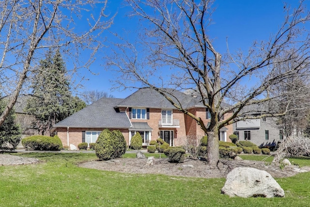 traditional-style house featuring brick siding, a front yard, and roof with shingles