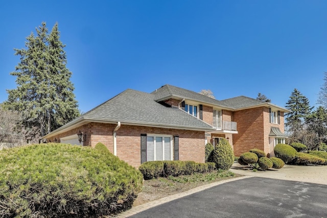 view of property exterior with roof with shingles, a balcony, a garage, and brick siding