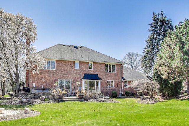back of house featuring a yard, brick siding, a patio, and roof with shingles