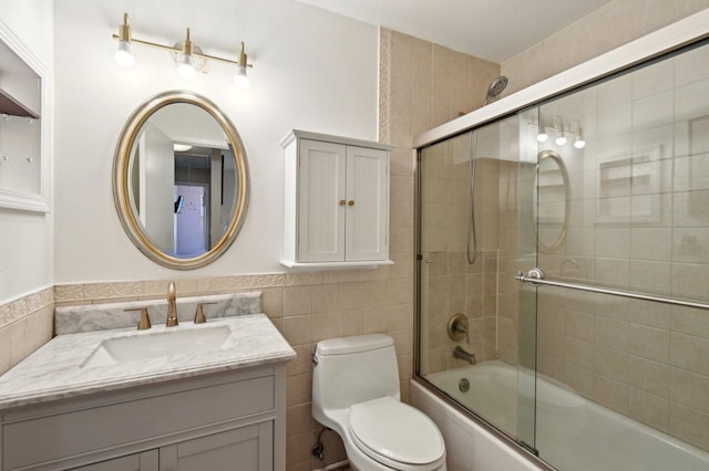 bathroom featuring combined bath / shower with glass door, toilet, vanity, and tile walls