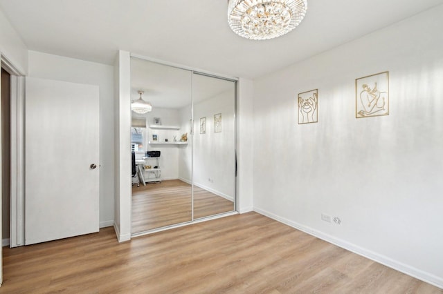 unfurnished bedroom with baseboards, wood finished floors, an inviting chandelier, and a closet