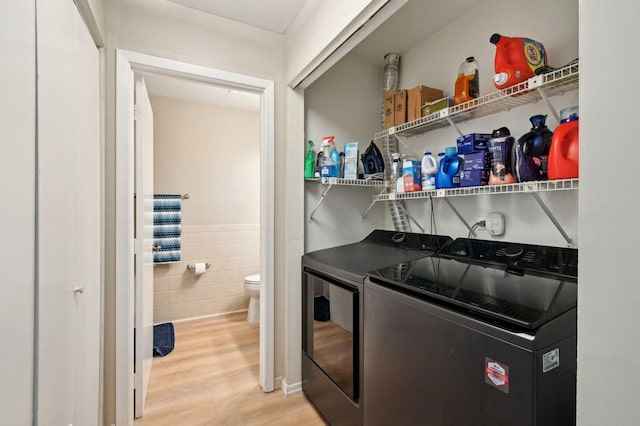 laundry room featuring a wainscoted wall, laundry area, wood finished floors, tile walls, and separate washer and dryer