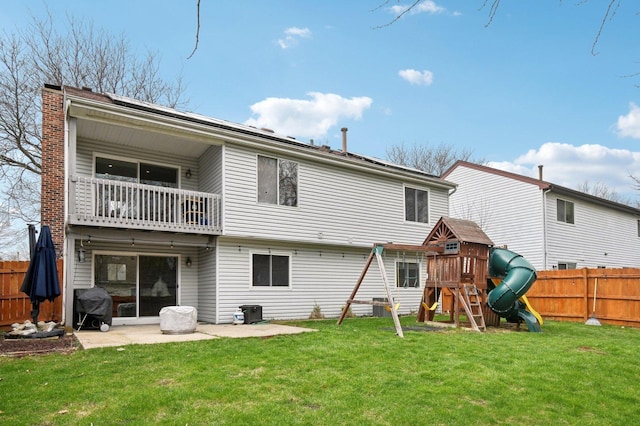 rear view of house featuring a lawn, a playground, a balcony, and fence