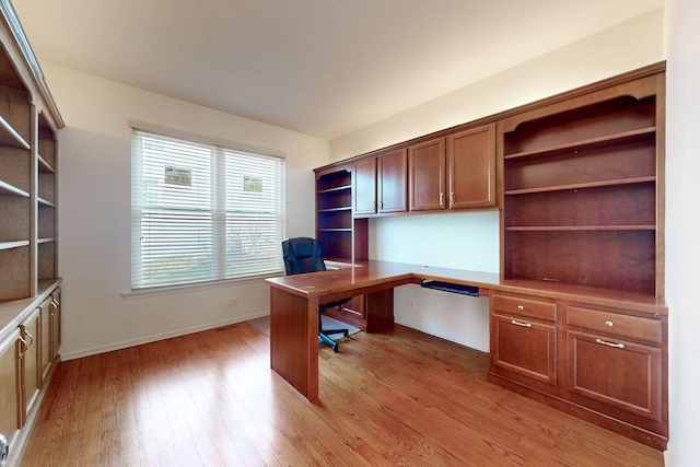 home office with built in study area, light wood-style floors, and baseboards