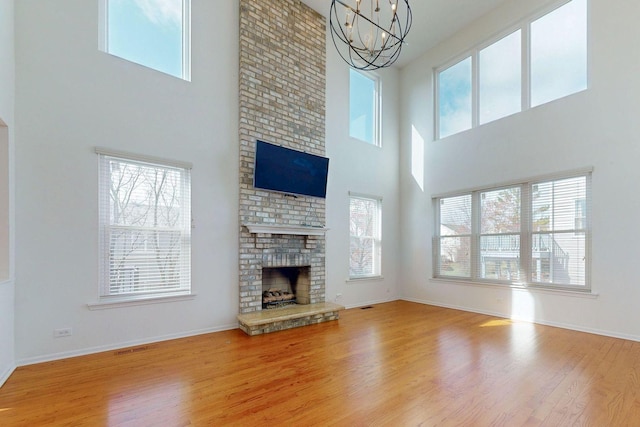 unfurnished living room featuring visible vents, baseboards, a brick fireplace, a chandelier, and wood finished floors