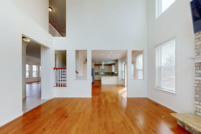 unfurnished living room featuring a towering ceiling, light wood-type flooring, baseboards, a fireplace, and stairway