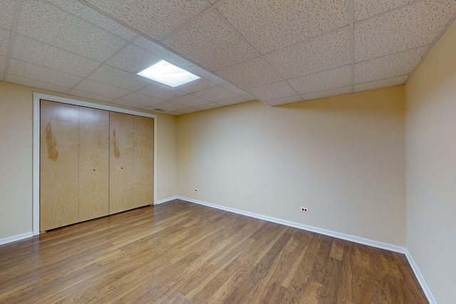 unfurnished bedroom featuring a closet, baseboards, a paneled ceiling, and wood finished floors