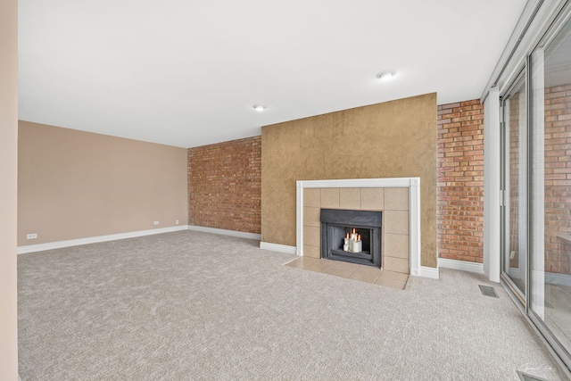 unfurnished living room with brick wall, a tiled fireplace, carpet, and baseboards