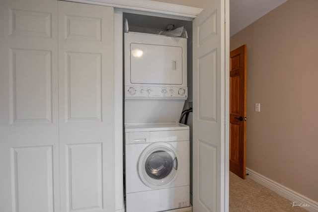 clothes washing area with laundry area, baseboards, stacked washer / drying machine, and light carpet
