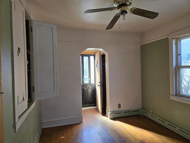 empty room with arched walkways, plenty of natural light, a ceiling fan, and wood finished floors