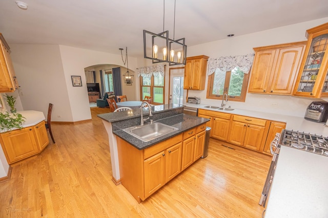 kitchen featuring arched walkways, a kitchen island with sink, a sink, and light wood-type flooring