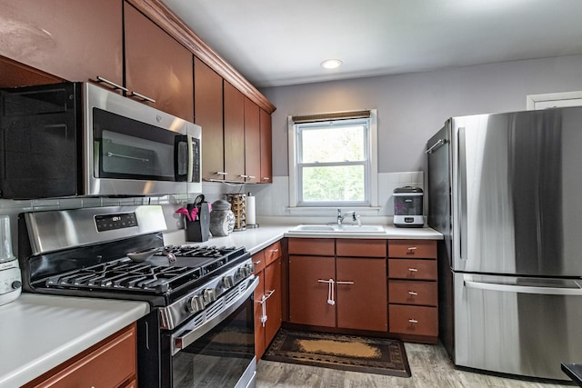 kitchen featuring stainless steel appliances, a sink, light wood finished floors, light countertops, and backsplash