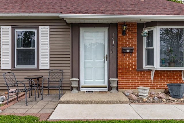 property entrance featuring brick siding and a shingled roof