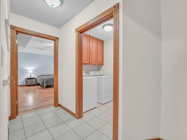clothes washing area featuring cabinet space, light tile patterned flooring, baseboards, and washing machine and dryer