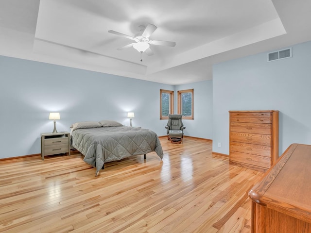 bedroom with visible vents, baseboards, a tray ceiling, a ceiling fan, and light wood finished floors