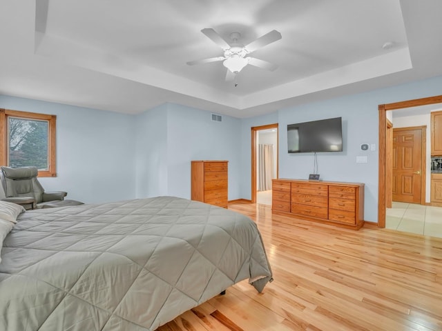 bedroom featuring ceiling fan, visible vents, light wood-type flooring, baseboards, and a tray ceiling