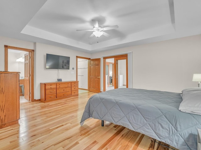 bedroom featuring a raised ceiling, baseboards, light wood-style flooring, and connected bathroom