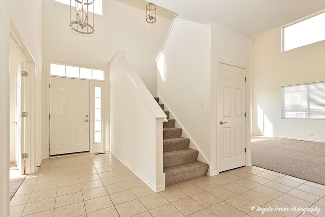 foyer entrance with light colored carpet, a towering ceiling, light tile patterned floors, and stairway