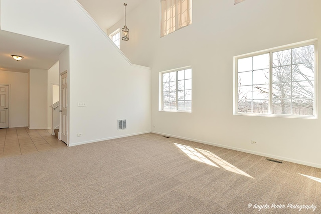 spare room with light colored carpet, a towering ceiling, visible vents, and light tile patterned floors