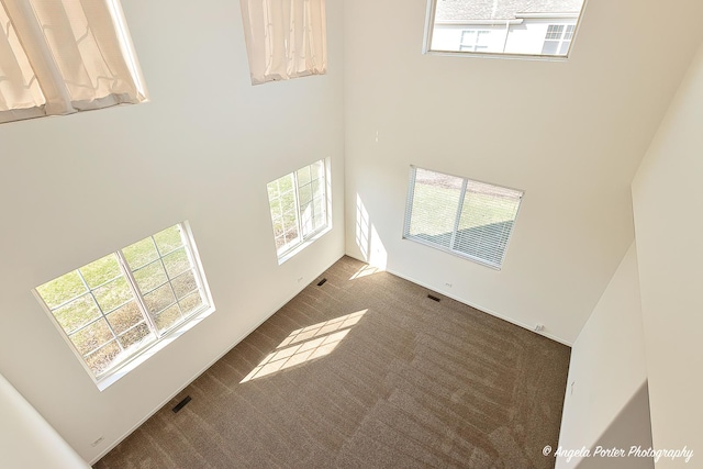 unfurnished living room featuring dark colored carpet, visible vents, and a towering ceiling