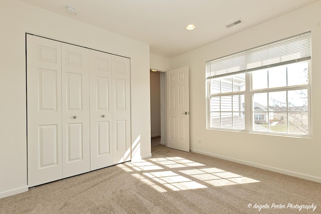 unfurnished bedroom featuring a closet, light colored carpet, baseboards, and visible vents