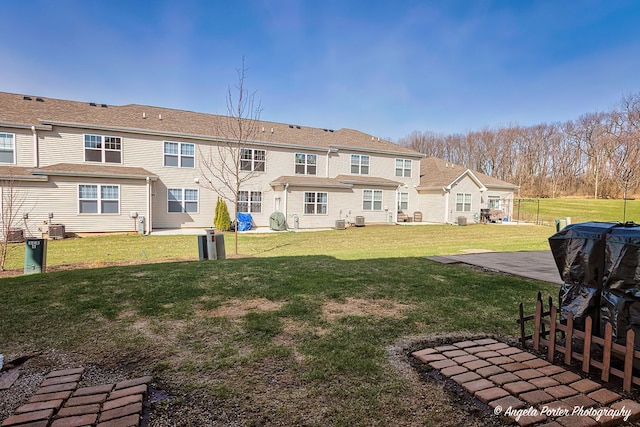 rear view of house with central AC unit, fence, and a lawn