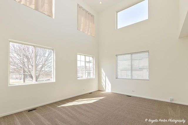 carpeted empty room with a towering ceiling, visible vents, and baseboards