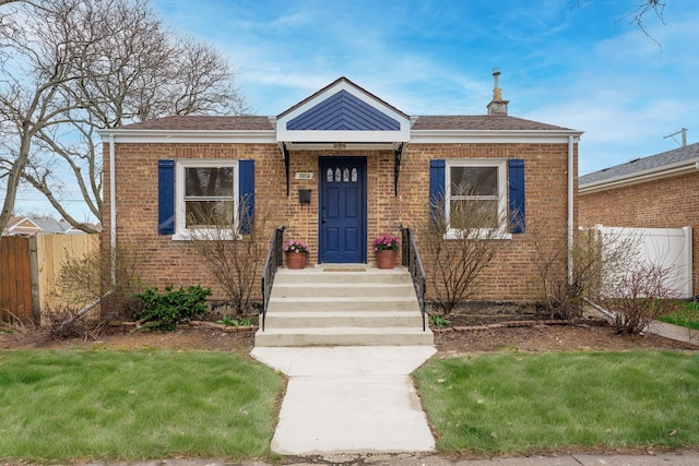 bungalow-style home featuring brick siding, fence, a shingled roof, and a chimney