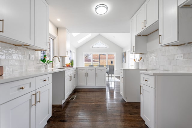 kitchen featuring a peninsula, dark wood-style floors, white cabinetry, lofted ceiling, and a sink