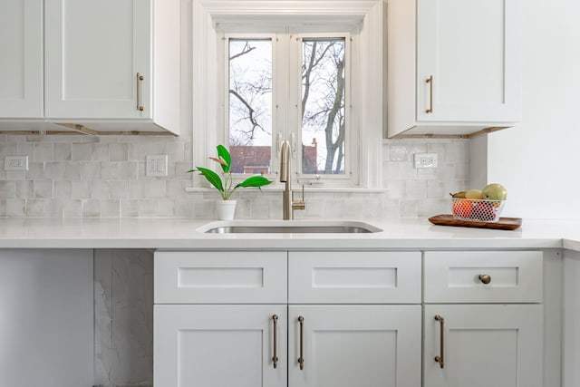 kitchen featuring light countertops, a sink, backsplash, and white cabinets
