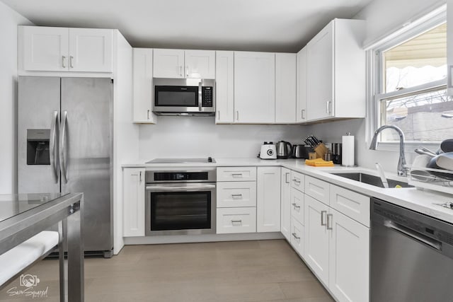 kitchen with light countertops, appliances with stainless steel finishes, a sink, and white cabinets